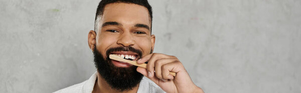 A cheerful man brushes his teeth while smiling at the camera.