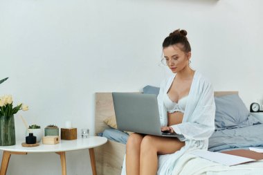 A young woman dressed in lingerie sits focused on her laptop in a stylish bedroom. clipart