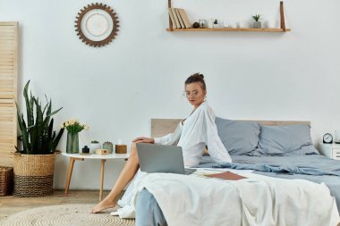 Stylish woman engages with laptop, surrounded by serene bedroom decor. clipart