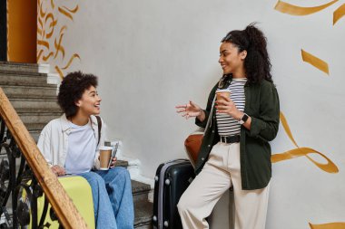 Two happy women share laughter and coffee while enjoying their travel adventure in a friendly hostel. clipart