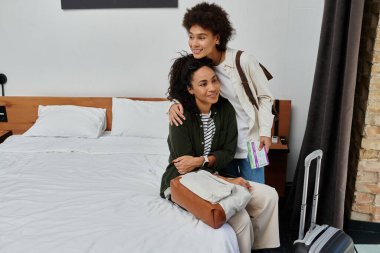 A happy couple celebrates their travels, sharing smiles and love while relaxing in their cozy hotel room. clipart