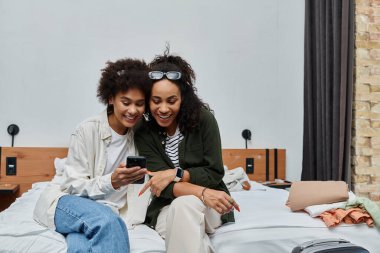 A cheerful couple embraces happiness while using smartphone in their hotel room together. clipart