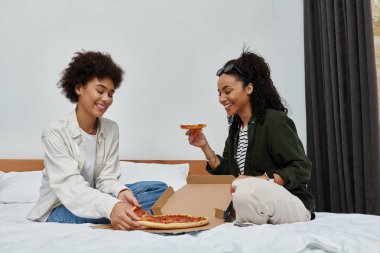 Mutlu bir çift pizza dilimlerini otel yatağında dinlenirken paylaşır, birlikte geçirdikleri zamanın tadını çıkarırlar..