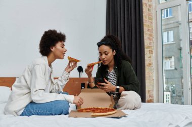 İki mutlu kadın otel odalarında dinlenirken pizza yiyip kahkaha atıyorlar..