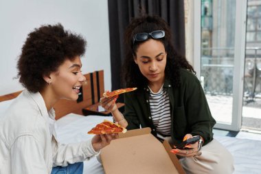 A happy couple shares pizza and laughter while relaxing together in their hotel room. clipart