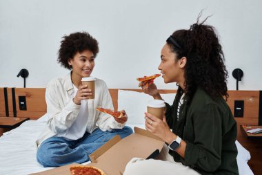 A happy couple shares laughter and pizza while sipping coffee in their inviting hotel retreat. clipart