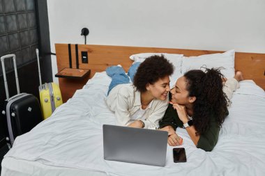 A happy couple relaxes together on a cozy bed, laughing and sharing moments in their hotel room. clipart