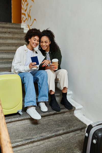 Two happy women share a moment while resting on hostel stairs, enjoying their travels and laughter.