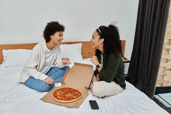 stock image A happy couple enjoys quality time together, laughing and sharing a pizza in their cozy hotel room.