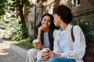 İki mutlu kadın dışarıda sohbet edip kahve yudumluyor, kahkahalarını paylaşıyor ve parkta güneşli bir günün tadını çıkarıyor..