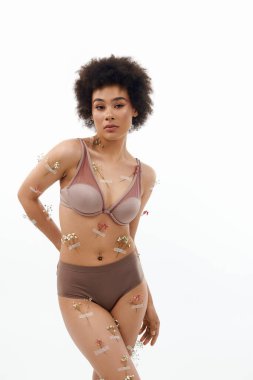 Kıvırcık saçlı, vücudu çiçek ve iç çamaşırlarıyla poz veren Afro-Amerikalı güzel bir kadın..