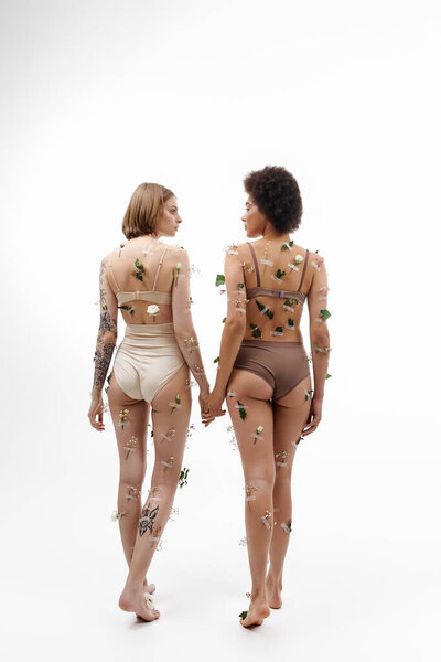 Two women share a tender moment, hands intertwined, decorated with delicate flowers.