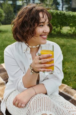 A pretty young woman relaxes in a summer picnic, sipping a cool drink and enjoying the sunny weather. clipart