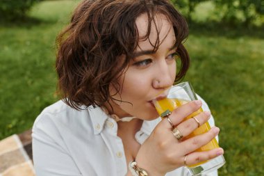 Beyaz gömlekli güzel bir kadın güneşli yaz pikniğinde ferahlatıcı bir içecek yudumluyor..