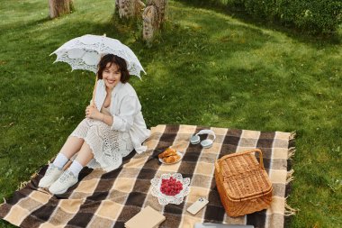 A pretty young woman relaxes in a summer picnic while enjoying delicious treats and warm sunshine. clipart