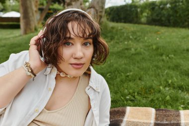 A young woman in a white shirt enjoys a peaceful picnic while listening to music outdoors.