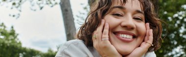 Beyaz gömlekli genç bir kadın güneşli bir yaz pikniğinde dinlenirken neşeyle gülümsüyor..