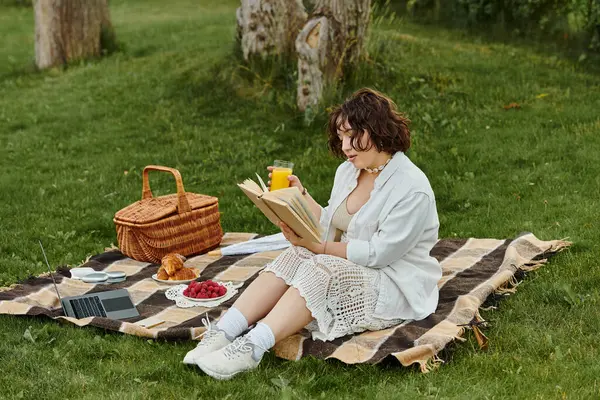 Güzel, genç bir kadın, yaz pikniği sırasında çimlerin üzerinde rahatça kitap okuyarak rahatlıyor..