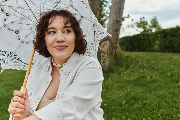 A young woman enjoys a summer picnic, resting with a lace umbrella while surrounded by nature.
