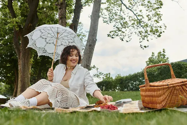 Neşeli genç bir kadın, güneşli bir yaz gününde, bir battaniyeye uzanıp, keyifli bir pikniğin tadını çıkarıyor..