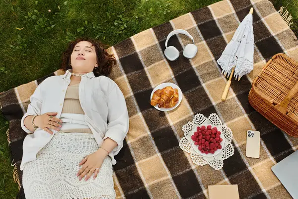 stock image A young woman enjoys a peaceful summer picnic, surrounded by delicious snacks and warm sunshine.