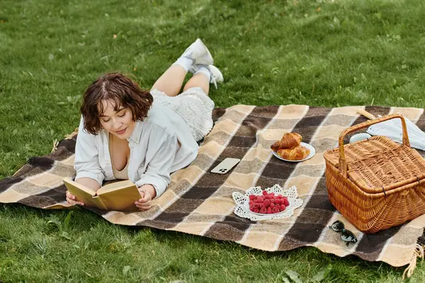 Genç bir kadın bir battaniyeye uzanır, bir kitaba gömülmüş, güneşin altında yaz ziyafetleriyle çevrili..