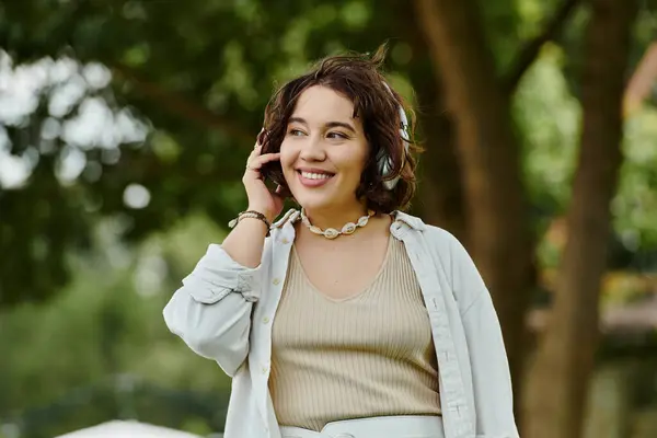 stock image A cheerful young woman in a white shirt embraces the tranquility of summer in a vibrant green park.