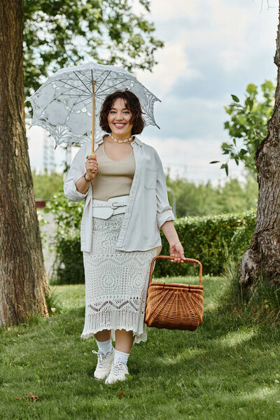 Веселая молодая женщина прогуливается по пышному парку, держа зонтик и корзину в солнечный летний день.