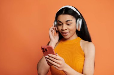 Bir kadın kulaklıkla müzik dinlerken ve telefonuna bakarken gülümsüyor..