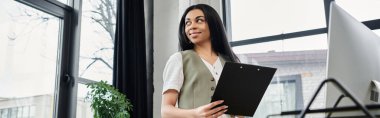 A professional woman stands confidently holding a clipboard in a modern office. clipart