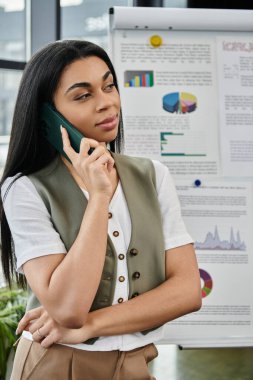 Kendine güvenen bir kadın çizelgeleri analiz ederken telefonla iletişim kuruyor..