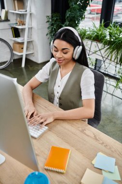 A young woman deeply engaged in her work while wearing headphones and smiling. clipart