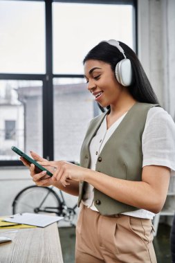 Telefonunu karıştırırken gülümseyen bir kadın müzik ve yaratıcılığa dalmış..