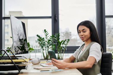 A woman smiles while using her phone in a stylish workspace filled with greenery. clipart