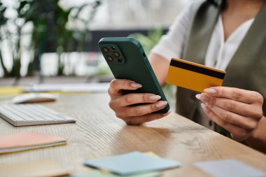 Kadın internet üzerinden alışveriş yapıyor, elinde bir kart ve akıllı telefon tutuyor..