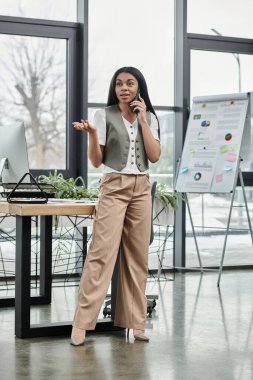 A poised woman discusses business matters while standing in a bright office. clipart