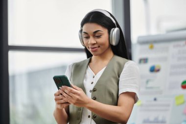 Müzik dinlerken, canlı bir çalışma alanında telefonunu karıştırırken gülümsüyor..
