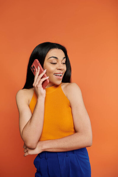 A cheerful young woman speaks animatedly on her phone, showcasing her radiant smile.