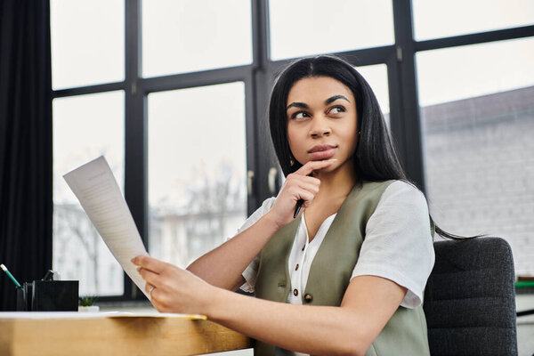 Pensive woman contemplates important documents at her workspace.