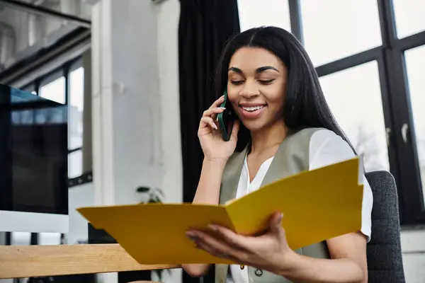 stock image A professional woman smiles while on a call, reviewing documents in her workspace.