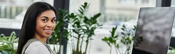 stock image Smiling woman surrounded by vibrant greenery in a bright workspace.