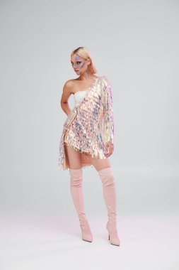 Genç bir kadın çarpıcı holografik kıyafetini basit bir arkaplanda sergiliyor..