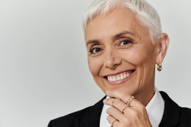 Kısa saçlı olgun bir kadın zarif bir şekilde gülümsüyor..