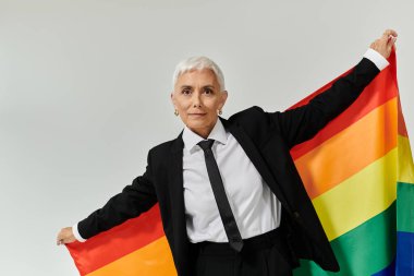 Olgun bir kadın gururla gökkuşağı bayrağı sergiler, kendine güven ve neşe saçar.