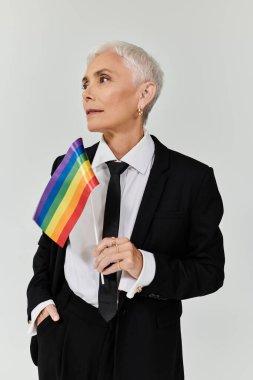 Olgun bir kadın gururla bir gökkuşağı bayrağı tutar, zarafet ve güç saçar..