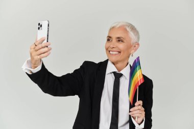 Şık bir kadın gökkuşağı bayrağı tutarken neşeyle selfie çeker..