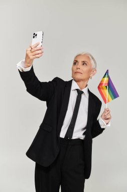 Kendine güvenen bir kadın gökkuşağı bayrağını tutar ve şık kıyafetler içinde selfie çeker..