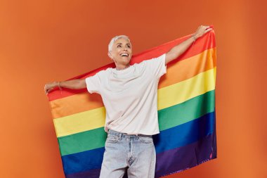 Gökkuşağı bayrağıyla gururu kucaklarken neşeli bir ifade.