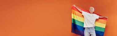 A mature woman radiates joy while holding a vibrant rainbow flag. clipart