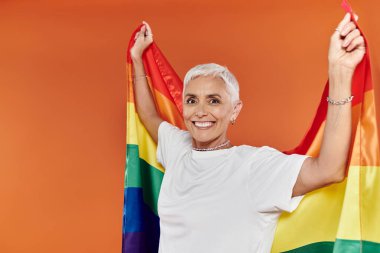 Olgun bir kadın gururla gökkuşağı bayrağını kucaklıyor, neşe ve güven saçıyor..